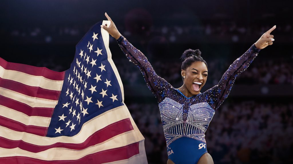 Photo de Simone Biles avec un grand sourire portant le drapeau USA de la main droite